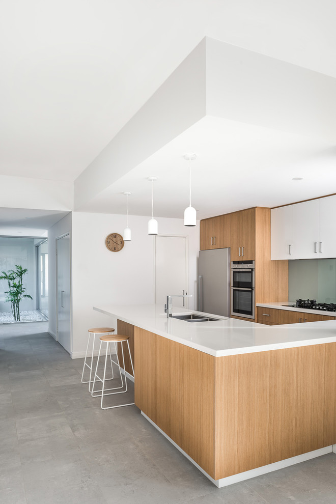 Inspiration for a contemporary u-shaped kitchen in Perth with light wood cabinets, quartz benchtops, glass sheet splashback, stainless steel appliances, ceramic floors, grey floor, white benchtop, a double-bowl sink, flat-panel cabinets, green splashback and a peninsula.