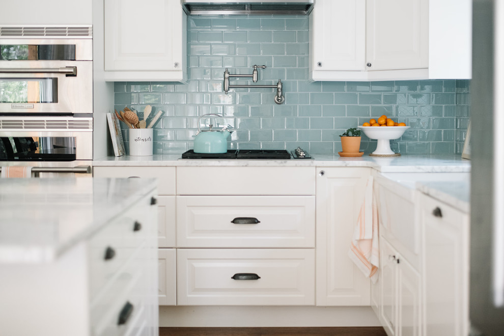 Inspiration for a mid-sized country l-shaped eat-in kitchen in Edmonton with a farmhouse sink, raised-panel cabinets, white cabinets, marble benchtops, blue splashback, glass tile splashback, stainless steel appliances, dark hardwood floors, with island, brown floor and white benchtop.