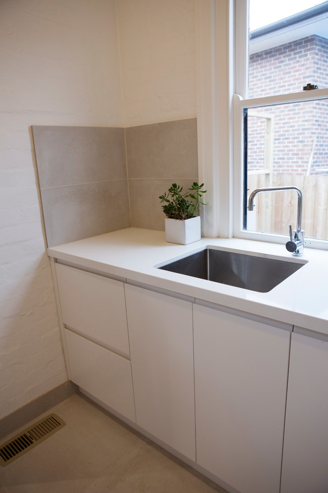Small contemporary l-shaped dedicated laundry room in Melbourne with an undermount sink, white cabinets, quartz benchtops, a side-by-side washer and dryer, flat-panel cabinets, white walls and concrete floors.