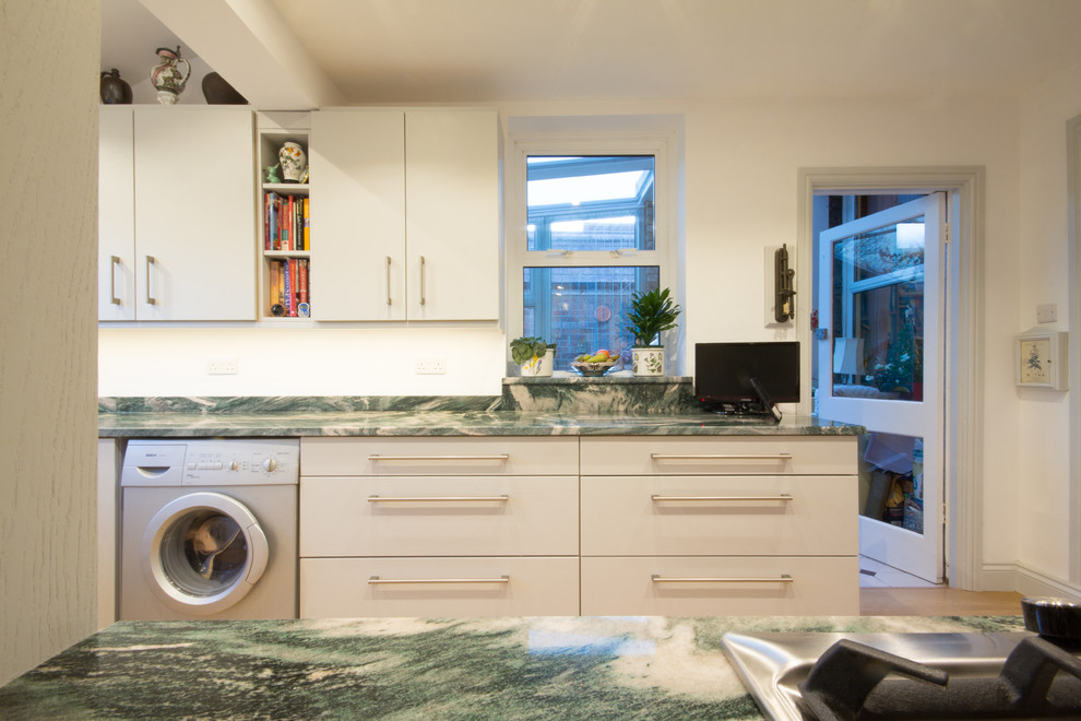 This is an example of a medium sized modern u-shaped enclosed kitchen in London with a built-in sink, flat-panel cabinets, grey cabinets, granite worktops, green splashback, stone slab splashback, integrated appliances, medium hardwood flooring and no island.