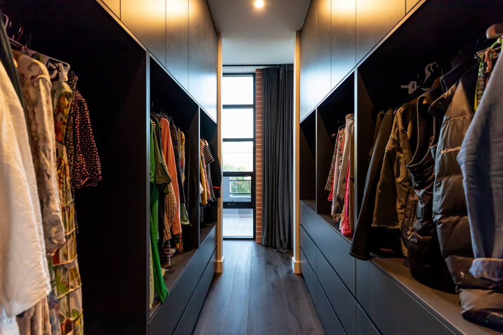 Ejemplo de armario vestidor unisex moderno pequeño con armarios con paneles lisos, puertas de armario negras y suelo de madera oscura