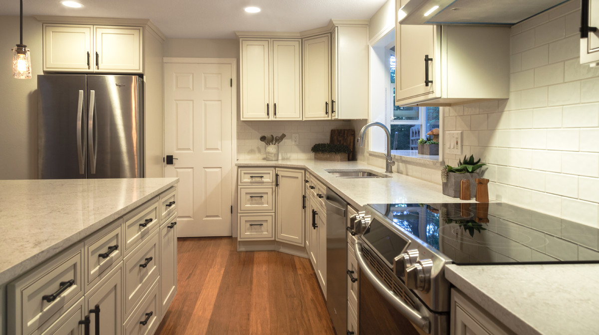 Mid-sized transitional l-shaped bamboo floor and brown floor eat-in kitchen photo in Seattle with a double-bowl sink, recessed-panel cabinets, quartz countertops, white backsplash, ceramic backsplash, stainless steel appliances and an island
