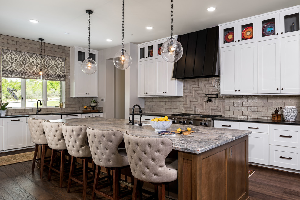 This is an example of a large country u-shaped kitchen in Other with a farmhouse sink, white cabinets, quartzite benchtops, beige splashback, brick splashback, stainless steel appliances, with island, brown floor, shaker cabinets and dark hardwood floors.