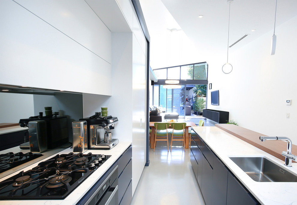 Contemporary open plan kitchen in Sydney with an undermount sink, flat-panel cabinets, white cabinets, granite benchtops, mirror splashback, stainless steel appliances, concrete floors and grey floor.