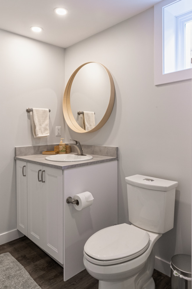 Photo of a mid-sized traditional 3/4 bathroom in Edmonton with shaker cabinets, white cabinets, an open shower, a two-piece toilet, grey walls, laminate floors, a drop-in sink, granite benchtops, grey floor, a hinged shower door, grey benchtops, a single vanity and a built-in vanity.