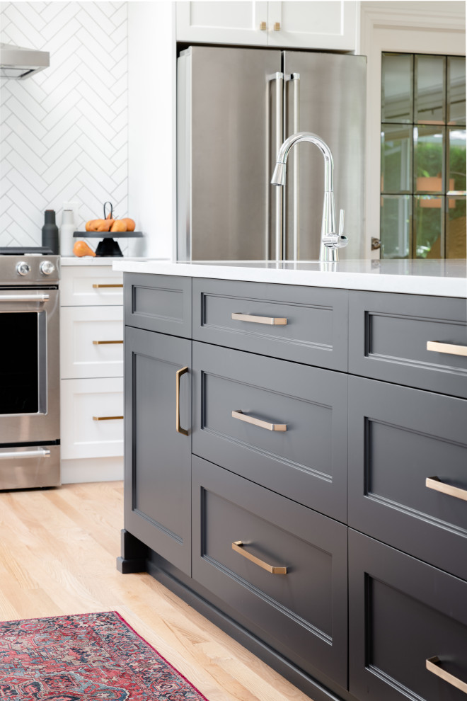 Example of a large transitional l-shaped light wood floor and beige floor open concept kitchen design in Vancouver with an undermount sink, recessed-panel cabinets, quartz countertops, white backsplash, ceramic backsplash, stainless steel appliances, an island, white countertops and gray cabinets