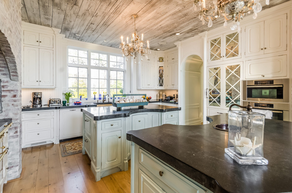 Photo of a large traditional u-shaped eat-in kitchen in Boston with a farmhouse sink, recessed-panel cabinets, medium hardwood floors, multiple islands, white cabinets, concrete benchtops, brown floor and black benchtop.