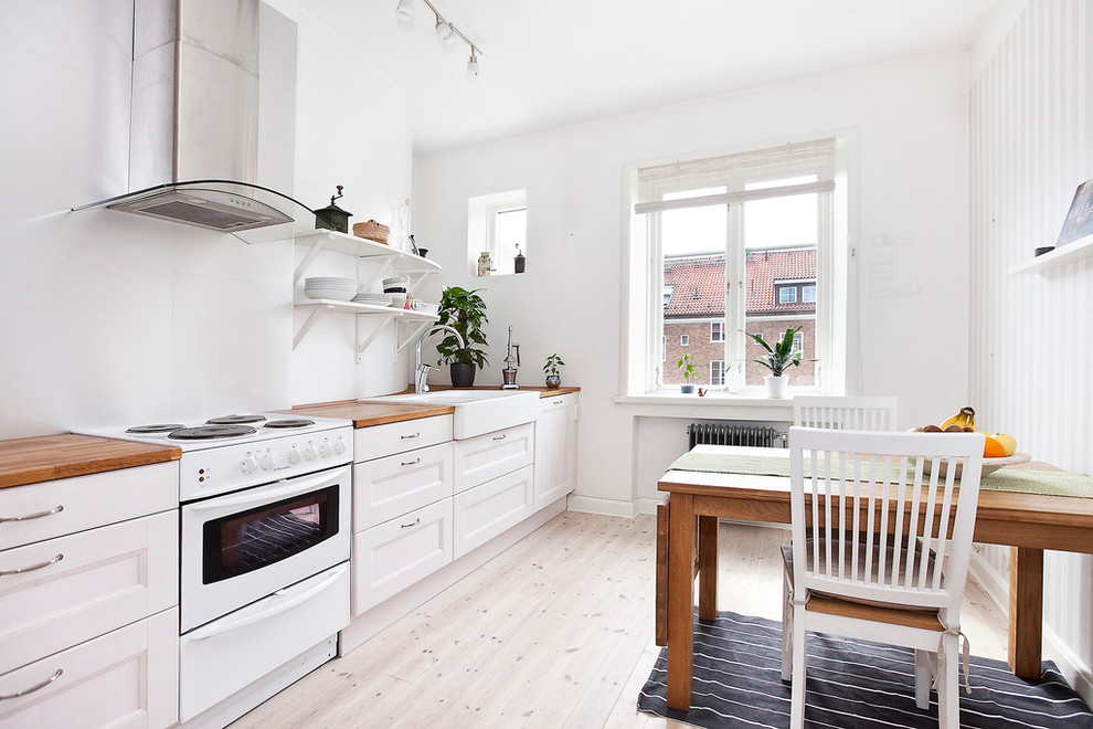 Mid-sized scandinavian single-wall eat-in kitchen in Malmo with a farmhouse sink, recessed-panel cabinets, white cabinets, wood benchtops, white splashback, stainless steel appliances, light hardwood floors and no island.