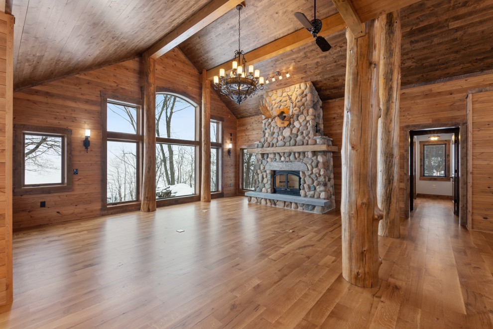 This is an example of a large country open concept living room in Minneapolis with brown walls, medium hardwood floors, a standard fireplace, a stone fireplace surround, brown floor, vaulted and wood walls.