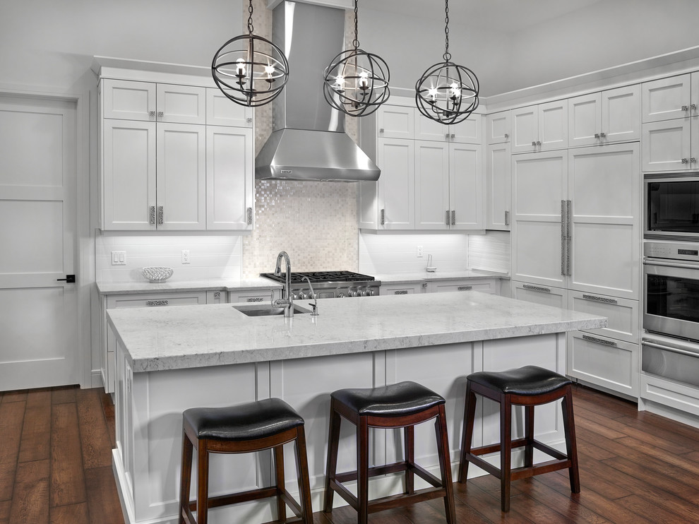 Example of a large arts and crafts u-shaped medium tone wood floor and brown floor eat-in kitchen design with an undermount sink, shaker cabinets, white cabinets, quartz countertops, white backsplash, subway tile backsplash, stainless steel appliances and an island