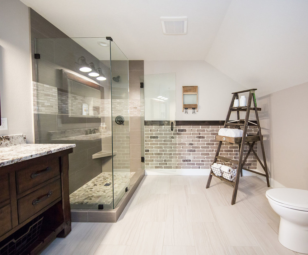 This is an example of a mid-sized country bathroom in Portland with furniture-like cabinets, dark wood cabinets, a corner shower, a one-piece toilet, grey walls, porcelain floors, an undermount sink, granite benchtops, grey floor, a hinged shower door and multi-coloured benchtops.