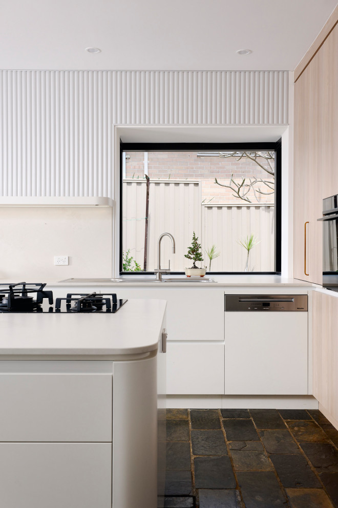 Inspiration for a large scandinavian l-shaped eat-in kitchen in Perth with a double-bowl sink, flat-panel cabinets, white cabinets, quartz benchtops, white splashback, engineered quartz splashback, black appliances, slate floors, with island, black floor and white benchtop.