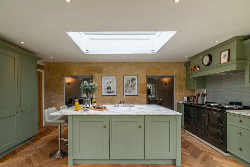 Mid-sized country separate kitchen in Gloucestershire with an integrated sink, shaker cabinets, green cabinets, quartzite benchtops, green splashback, subway tile splashback, black appliances, dark hardwood floors, with island, brown floor and white benchtop.