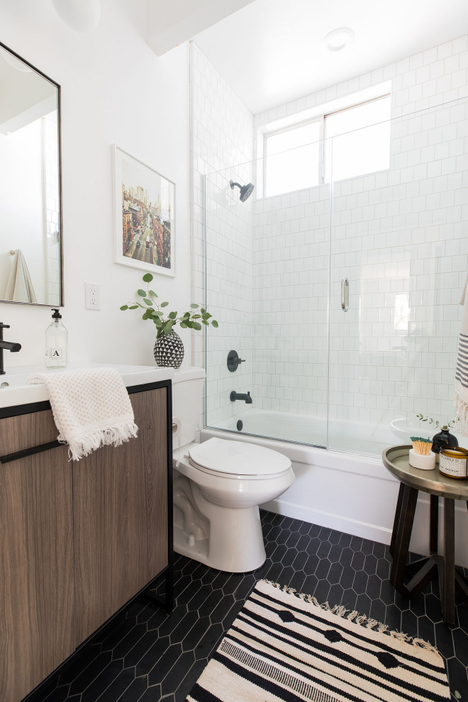 Midcentury 3/4 bathroom in Sacramento with flat-panel cabinets, dark wood cabinets, an alcove tub, a shower/bathtub combo, a two-piece toilet, white tile, white walls, a console sink and black floor.