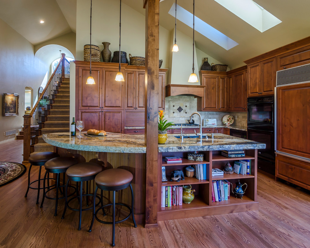 This is an example of a mid-sized traditional single-wall eat-in kitchen in Denver with an undermount sink, raised-panel cabinets, medium wood cabinets, granite benchtops, blue splashback, stone tile splashback, panelled appliances, medium hardwood floors and with island.