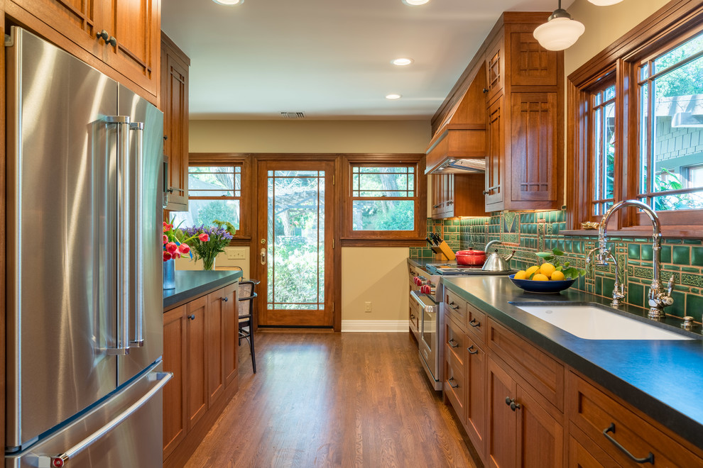 Inspiration for a mid-sized craftsman galley medium tone wood floor and brown floor enclosed kitchen remodel in Los Angeles with an undermount sink, shaker cabinets, dark wood cabinets, granite countertops, green backsplash, ceramic backsplash and paneled appliances