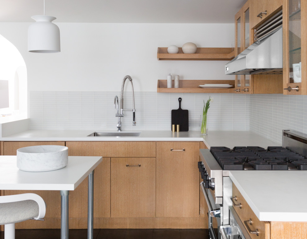Photo of a small modern l-shaped separate kitchen in New York with a drop-in sink, flat-panel cabinets, light wood cabinets, quartz benchtops, white splashback, ceramic splashback, stainless steel appliances, dark hardwood floors, with island and black benchtop.