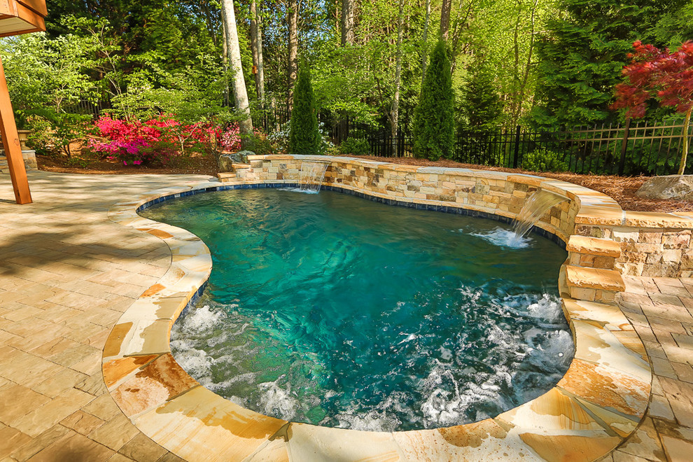 Design ideas for a large traditional backyard custom-shaped natural pool in Atlanta with brick pavers and a water feature.