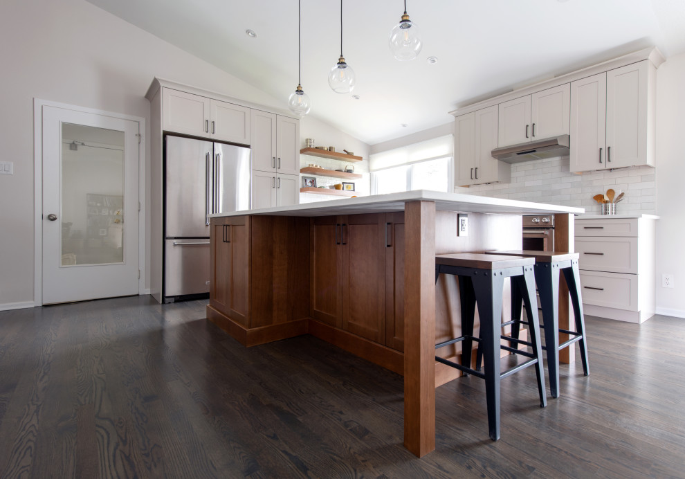 Mid-sized transitional l-shaped medium tone wood floor, gray floor and vaulted ceiling open concept kitchen photo in Ottawa with a double-bowl sink, shaker cabinets, gray cabinets, quartz countertops, white backsplash, subway tile backsplash, stainless steel appliances, an island and white countertops