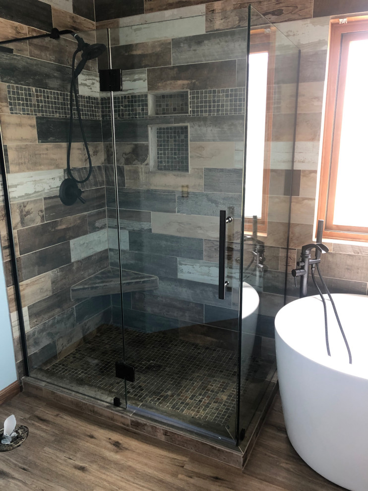 Photo of a mid-sized country master bathroom in Denver with a freestanding tub, a corner shower, brown tile, porcelain tile, vinyl floors, brown floor, a hinged shower door and a freestanding vanity.