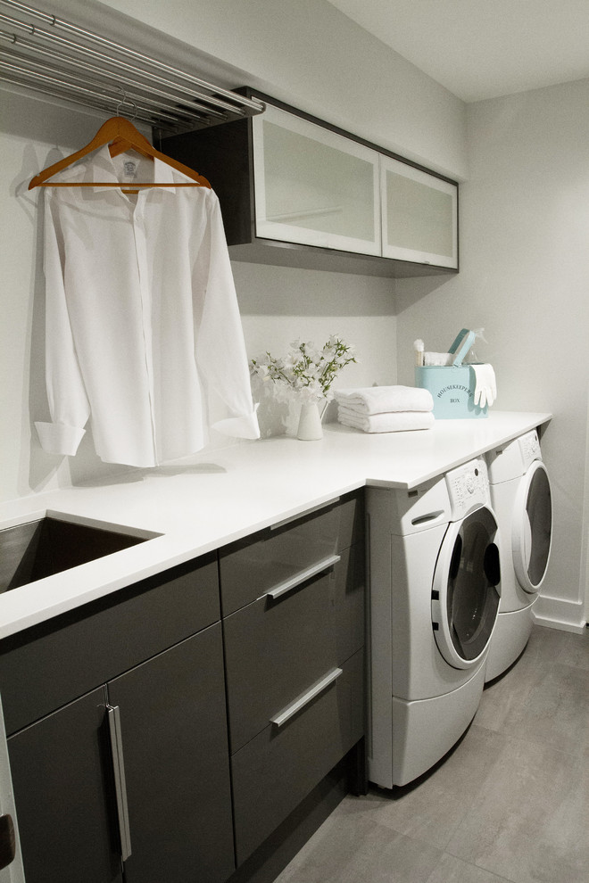 Photo of a modern galley laundry room in Vancouver with vinyl floors, an undermount sink, a side-by-side washer and dryer, quartz benchtops, grey cabinets and flat-panel cabinets.