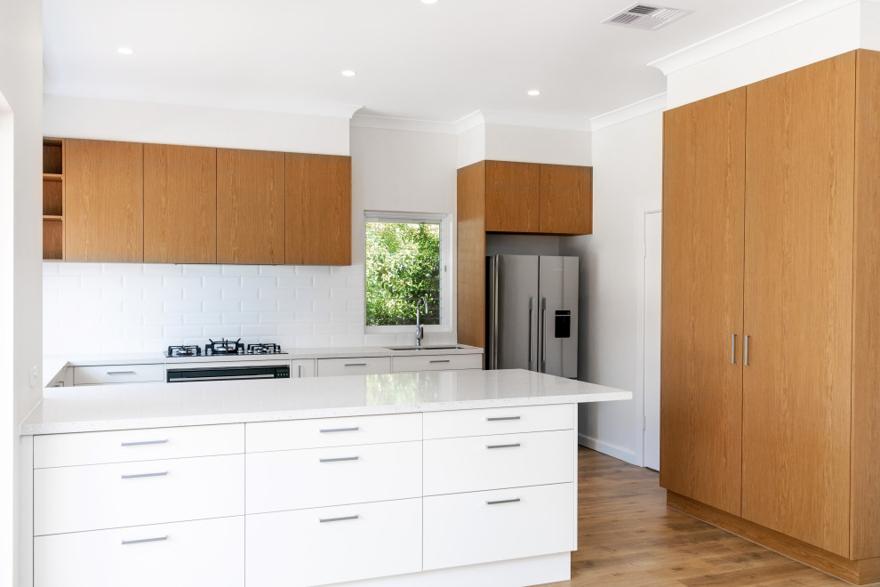 Eat-in kitchen - large 1950s u-shaped light wood floor and brown floor eat-in kitchen idea in Adelaide with a double-bowl sink, flat-panel cabinets, medium tone wood cabinets, quartz countertops, white backsplash, ceramic backsplash, black appliances, an island and white countertops