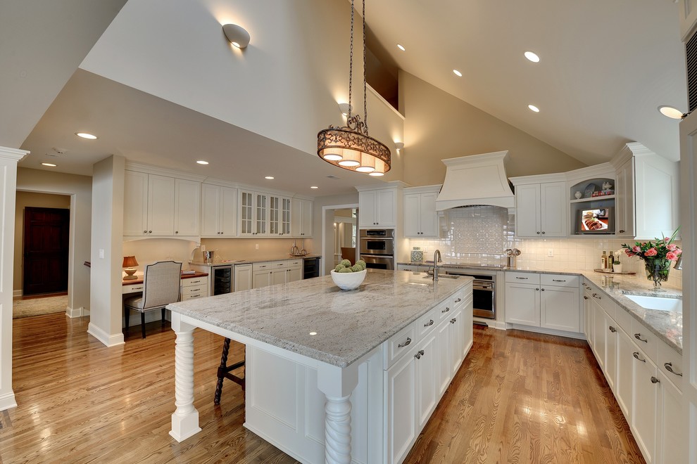 Photo of a large traditional l-shaped eat-in kitchen in Minneapolis with an undermount sink, white cabinets, white splashback, with island, white appliances, ceramic splashback, granite benchtops, brown floor, recessed-panel cabinets and medium hardwood floors.