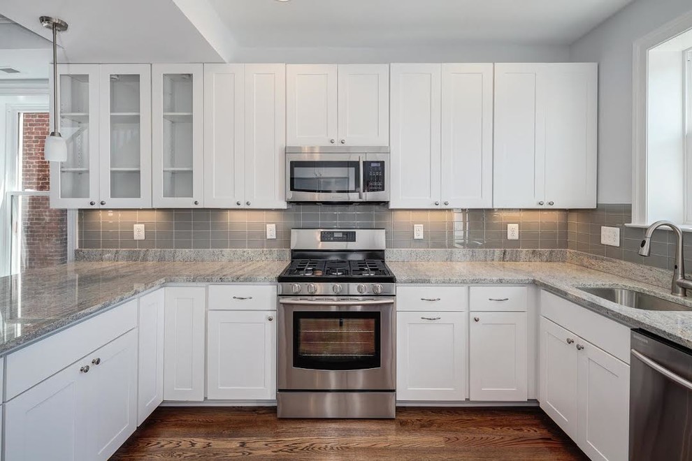 Open concept kitchen - mid-sized transitional u-shaped light wood floor and beige floor open concept kitchen idea in Los Angeles with an undermount sink, shaker cabinets, white cabinets, glass countertops, gray backsplash, glass sheet backsplash, stainless steel appliances and a peninsula