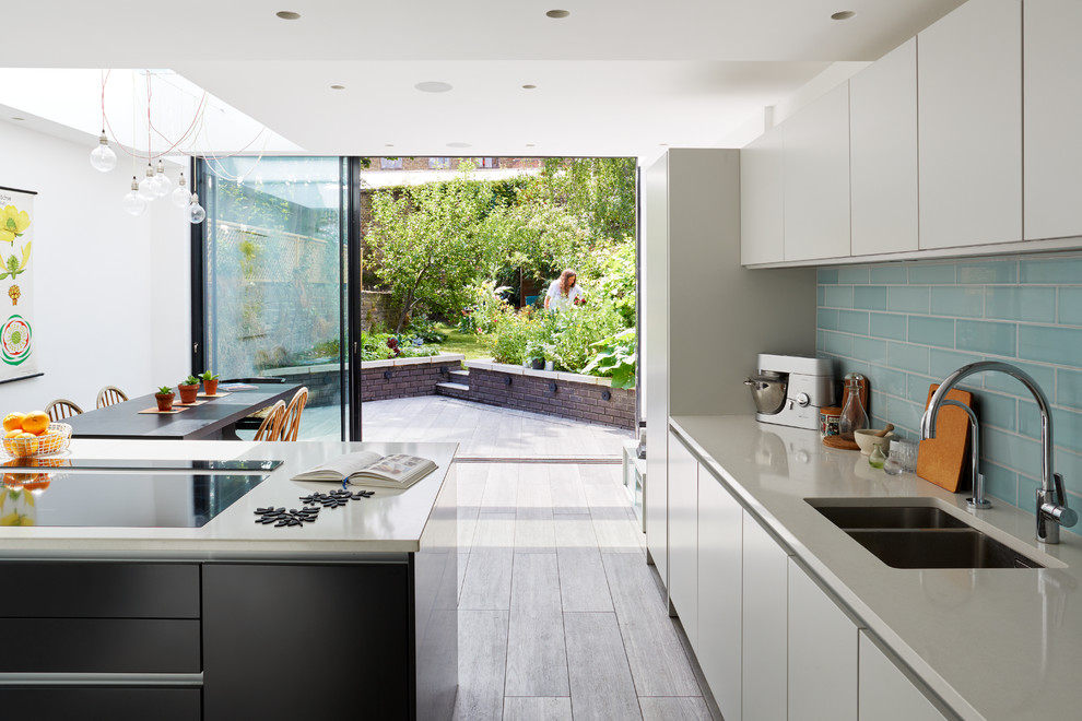 This is an example of a contemporary eat-in kitchen in London with a double-bowl sink, flat-panel cabinets, white cabinets, blue splashback, subway tile splashback and with island.