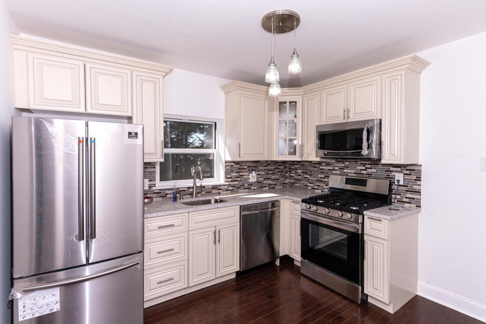 Modern inredning av ett litet vit vitt kök, med en nedsänkt diskho, skåp i shakerstil, vita skåp, bänkskiva i kvartsit, grått stänkskydd, stänkskydd i marmor, rostfria vitvaror, mörkt trägolv, en köksö och brunt golv