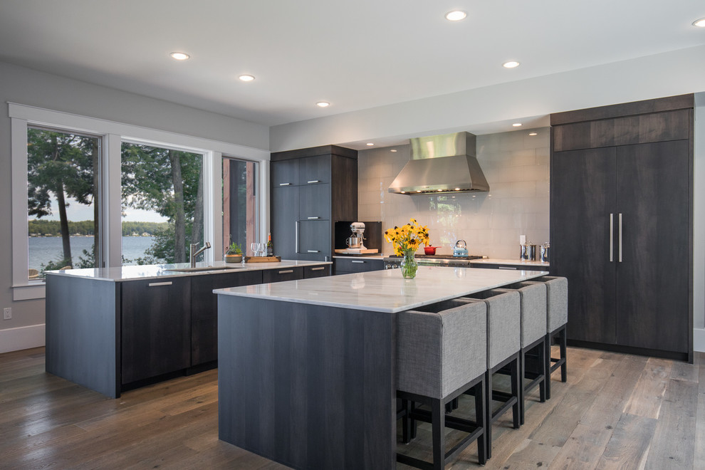 Photo of a contemporary single-wall open plan kitchen in Boston with an undermount sink, flat-panel cabinets, distressed cabinets, white splashback, panelled appliances, medium hardwood floors, multiple islands and grey floor.