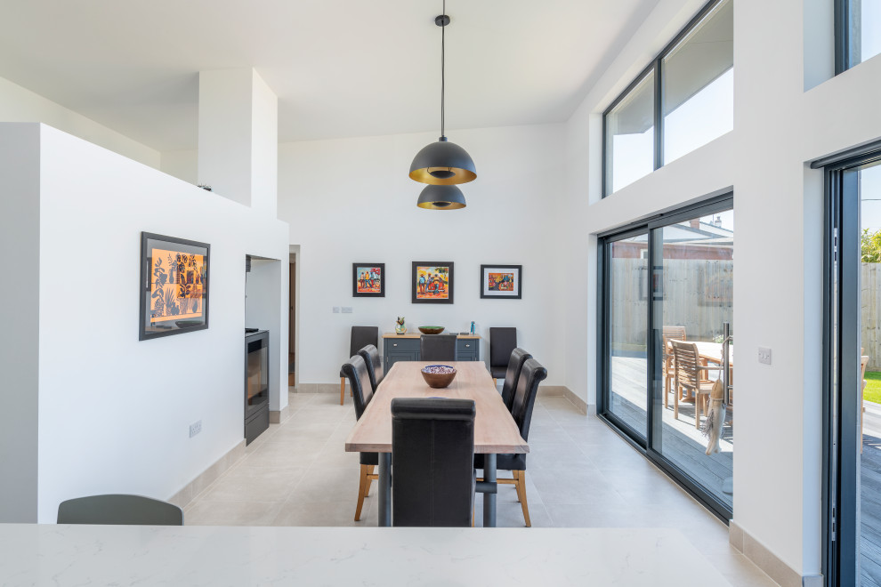 This is an example of a large contemporary open plan dining in Cornwall with white walls, ceramic floors, a two-sided fireplace, a plaster fireplace surround and beige floor.