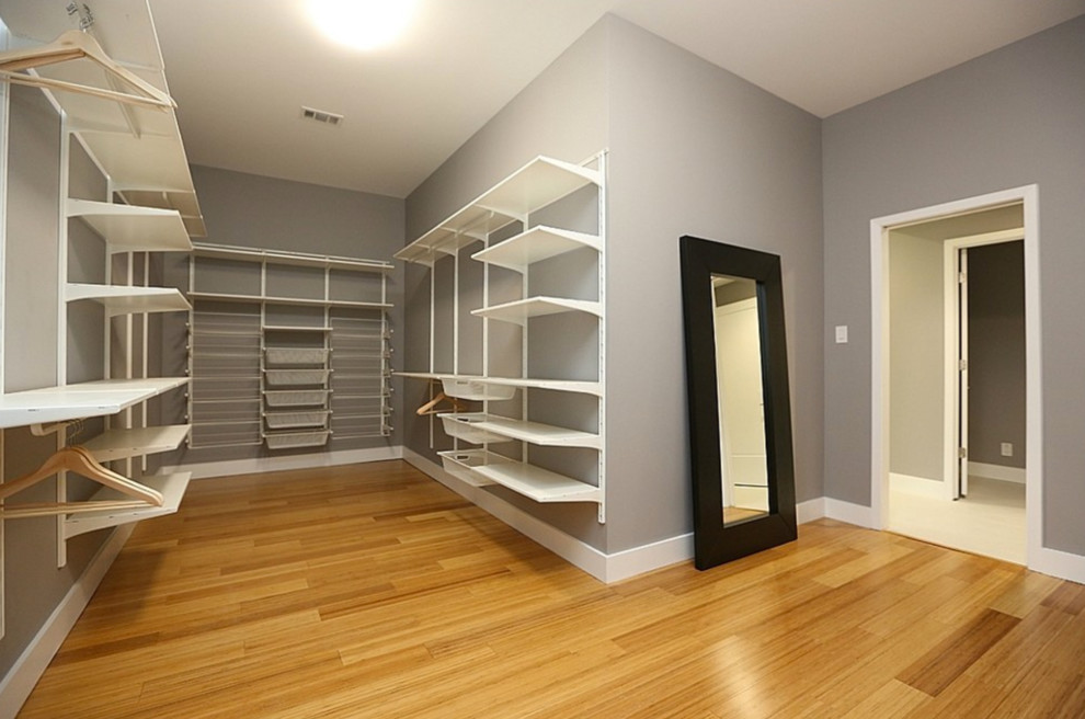 Large modern gender-neutral walk-in wardrobe in Dallas with bamboo floors, open cabinets and white cabinets.
