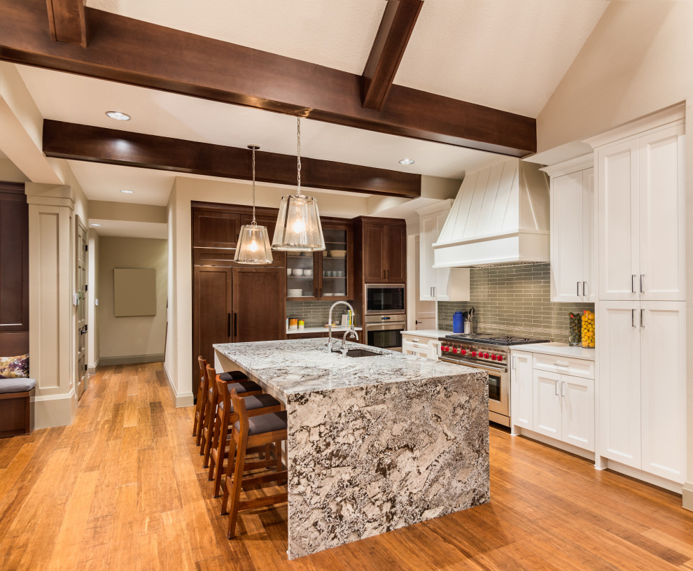 Inspiration for a large transitional l-shaped medium tone wood floor, brown floor, exposed beam and vaulted ceiling open concept kitchen remodel in Los Angeles with an undermount sink, shaker cabinets, white cabinets, green backsplash, stainless steel appliances, an island, gray countertops, granite countertops and subway tile backsplash