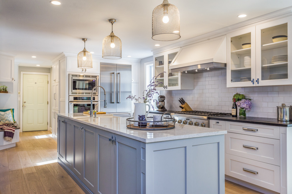 Inspiration for a transitional galley eat-in kitchen in Manchester with a farmhouse sink, shaker cabinets, white cabinets, soapstone benchtops, white splashback, ceramic splashback, stainless steel appliances, light hardwood floors, with island and brown floor.