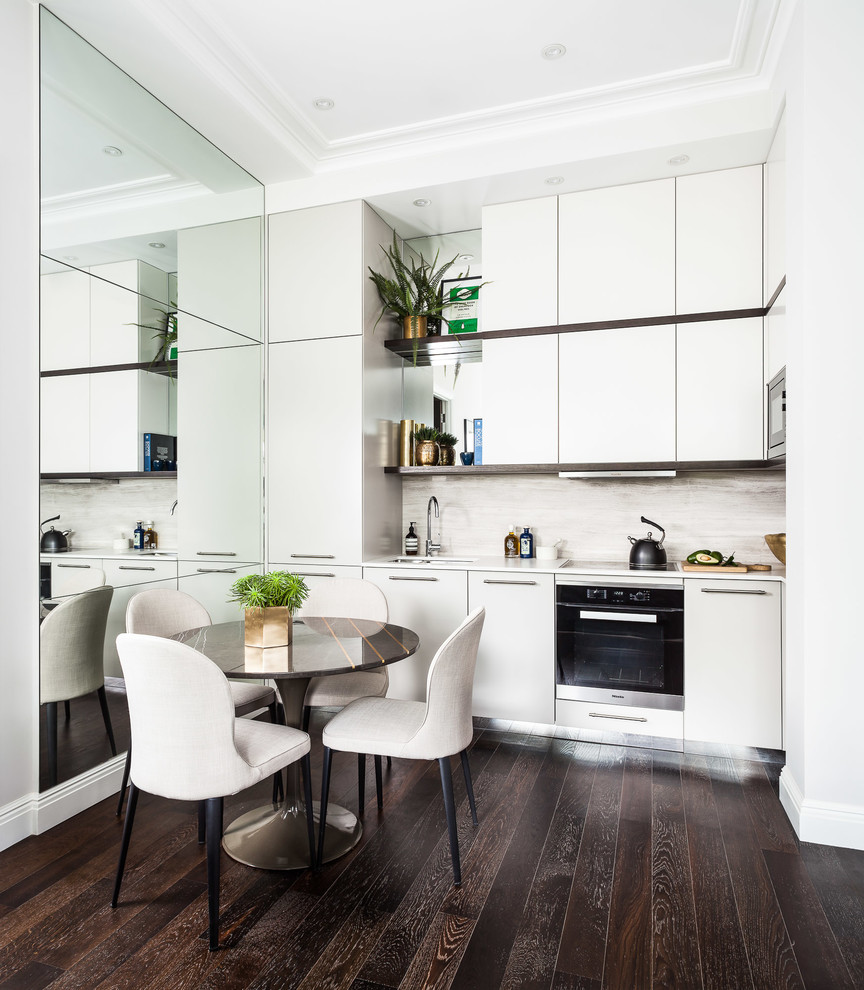 This is an example of a small contemporary single-wall open plan kitchen in London with an integrated sink, flat-panel cabinets, beige cabinets, quartz benchtops, beige splashback, limestone splashback and black appliances.