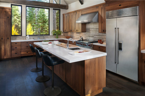 Warm modern kitchen with walnut kitchen cabinets, white island countertop and large windows overlooking a forest view