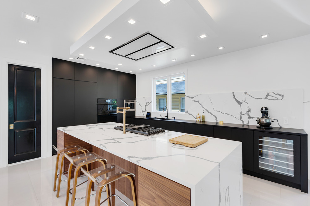 Inspiration for an expansive contemporary kitchen in New York with a double-bowl sink, flat-panel cabinets, white splashback, stone slab splashback, with island, white floor, black benchtop and black appliances.