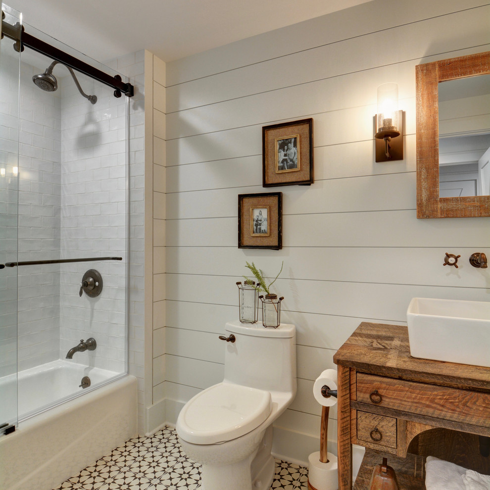 Photo of a country kids bathroom in Chicago with distressed cabinets, a shower/bathtub combo, a one-piece toilet, gray tile, ceramic tile, white walls, ceramic floors, wood benchtops, white floor and a hinged shower door.