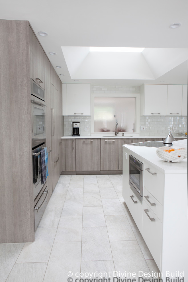 Design ideas for a contemporary l-shaped eat-in kitchen in Boston with an undermount sink, flat-panel cabinets, grey cabinets, grey splashback, subway tile splashback, stainless steel appliances, porcelain floors and with island.