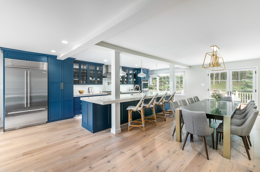 This is an example of an expansive contemporary single-wall eat-in kitchen in DC Metro with an undermount sink, glass-front cabinets, blue cabinets, quartz benchtops, white splashback, ceramic splashback, stainless steel appliances, light hardwood floors, with island, beige floor and white benchtop.