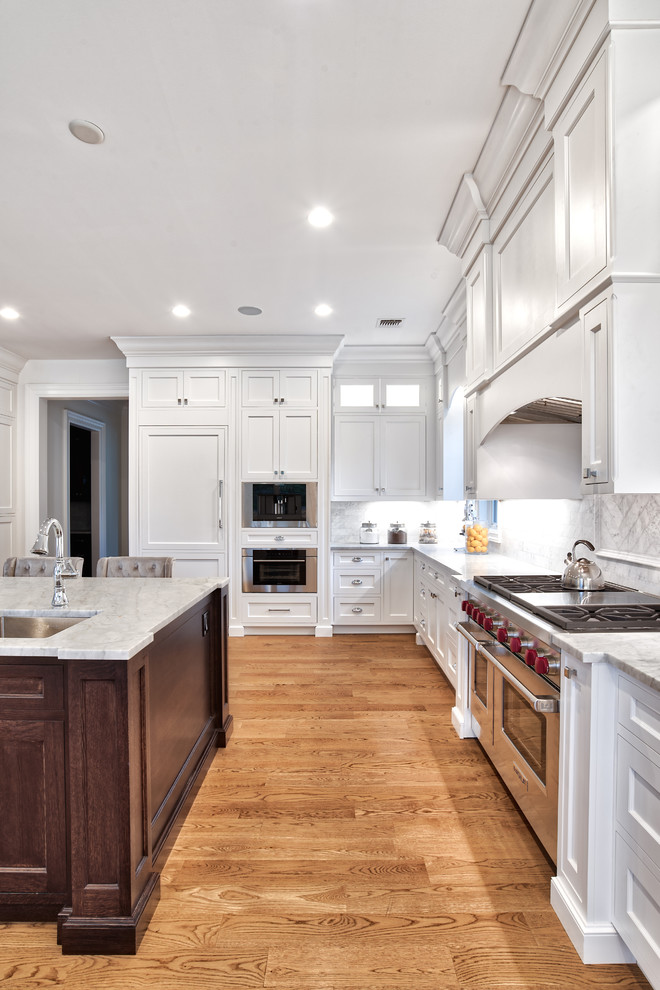 Inspiration for a huge transitional u-shaped light wood floor and brown floor open concept kitchen remodel in New York with a farmhouse sink, shaker cabinets, white cabinets, quartzite countertops, white backsplash, porcelain backsplash, paneled appliances, an island and multicolored countertops