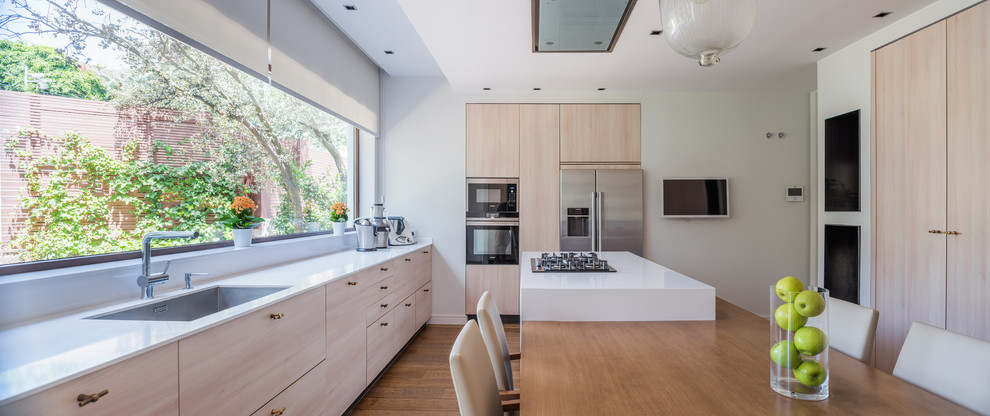 Inspiration for a contemporary u-shaped separate kitchen in Madrid with a single-bowl sink, flat-panel cabinets, light wood cabinets, window splashback, stainless steel appliances, dark hardwood floors, with island, brown floor and white benchtop.