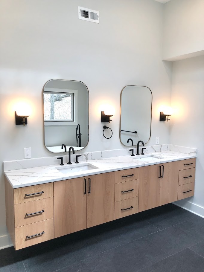 This is an example of a large scandinavian master bathroom in New York with flat-panel cabinets, light wood cabinets, a freestanding tub, a corner shower, a two-piece toilet, white tile, porcelain tile, white walls, porcelain floors, an undermount sink, quartzite benchtops, black floor, a hinged shower door and white benchtops.