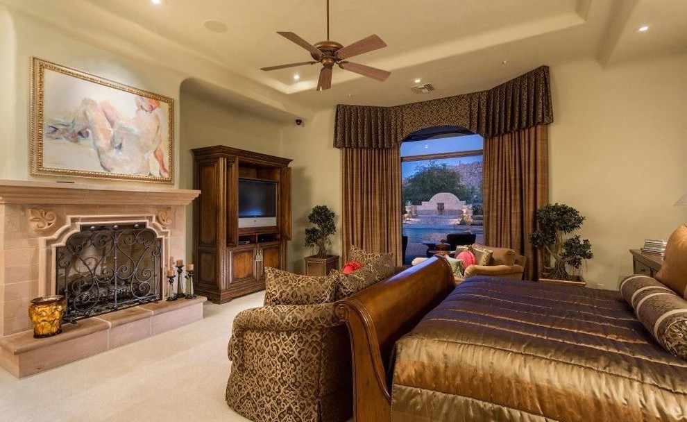 This is an example of an expansive traditional master bedroom in Phoenix with beige walls, travertine floors, a standard fireplace and a tile fireplace surround.