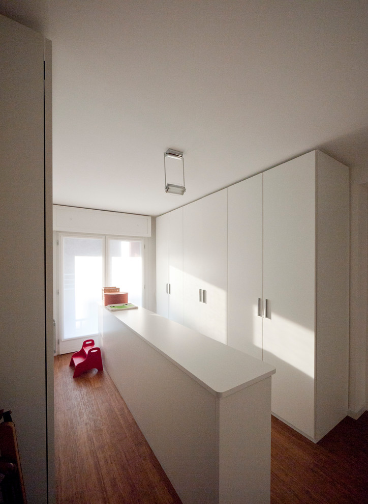 This is an example of a large modern gender-neutral built-in wardrobe in Milan with flat-panel cabinets, white cabinets and bamboo floors.