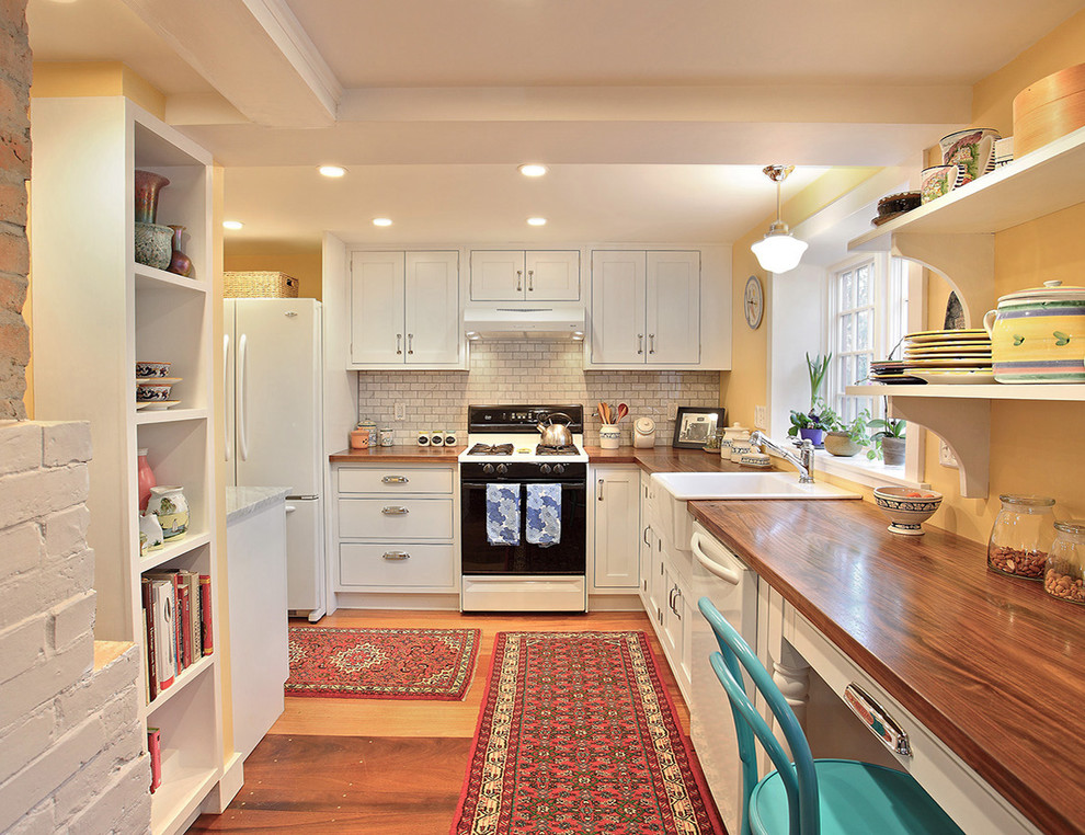 Design ideas for a traditional l-shaped separate kitchen in Boston with a farmhouse sink, white appliances, wood benchtops, white cabinets, white splashback and subway tile splashback.