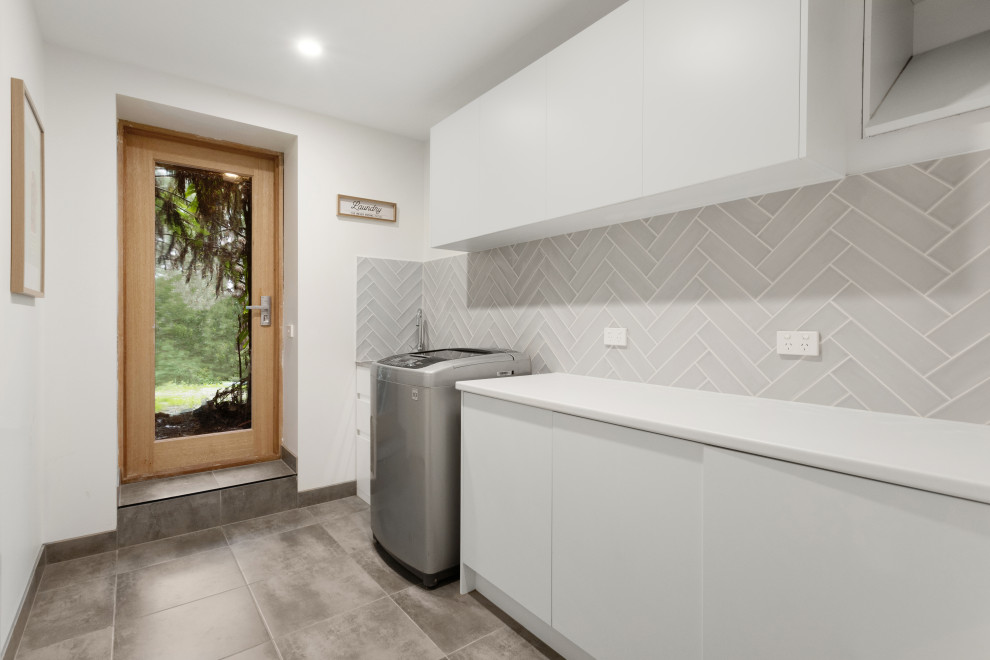 Mid-sized contemporary galley laundry room in Melbourne with flat-panel cabinets, white cabinets, laminate benchtops, grey splashback, subway tile splashback, grey walls, porcelain floors, grey floor and white benchtop.