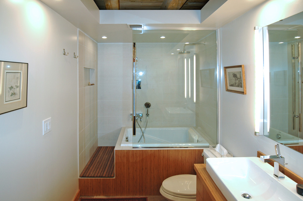 Inspiration for a mid-sized contemporary master bathroom in Other with a vessel sink, flat-panel cabinets, light wood cabinets, wood benchtops, a japanese tub, a shower/bathtub combo, a two-piece toilet, beige tile, stone slab, white walls and concrete floors.