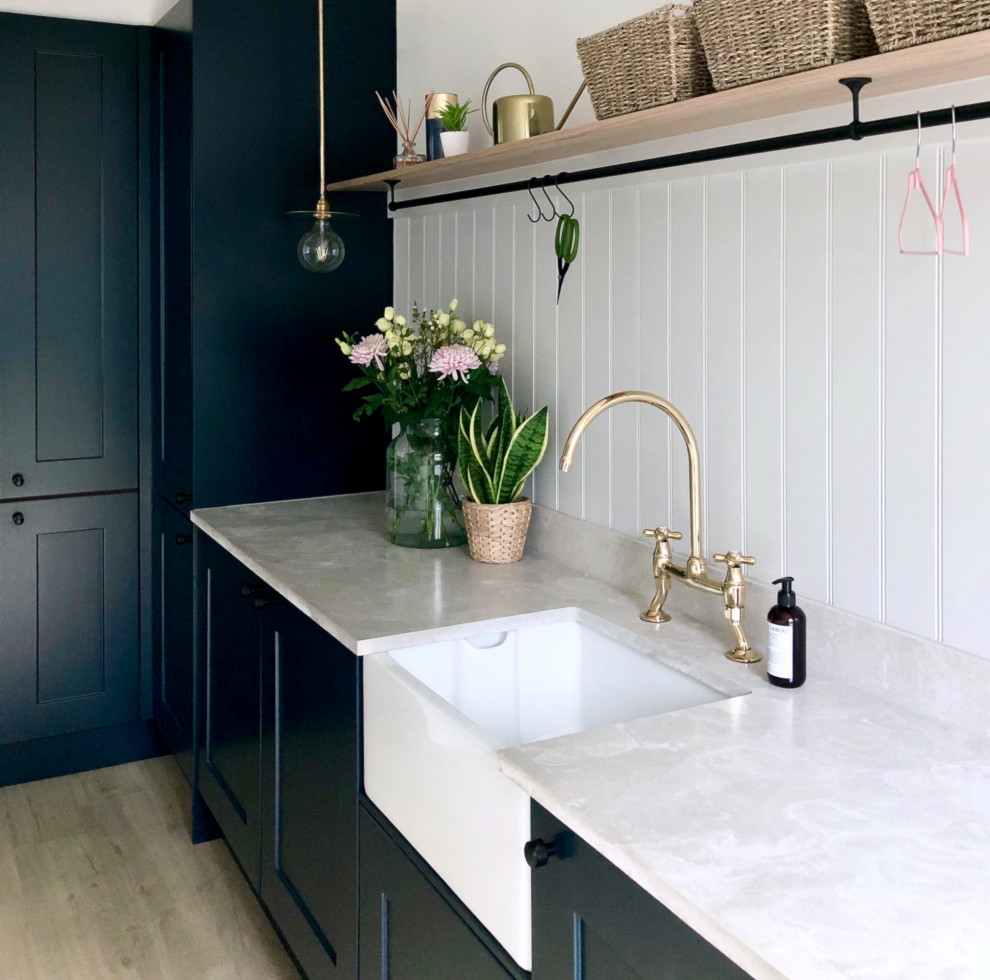 Photo of a small traditional single-wall utility room in Other with a farmhouse sink, shaker cabinets, blue cabinets, grey walls, laminate floors, an integrated washer and dryer, beige floor, grey benchtop and planked wall panelling.